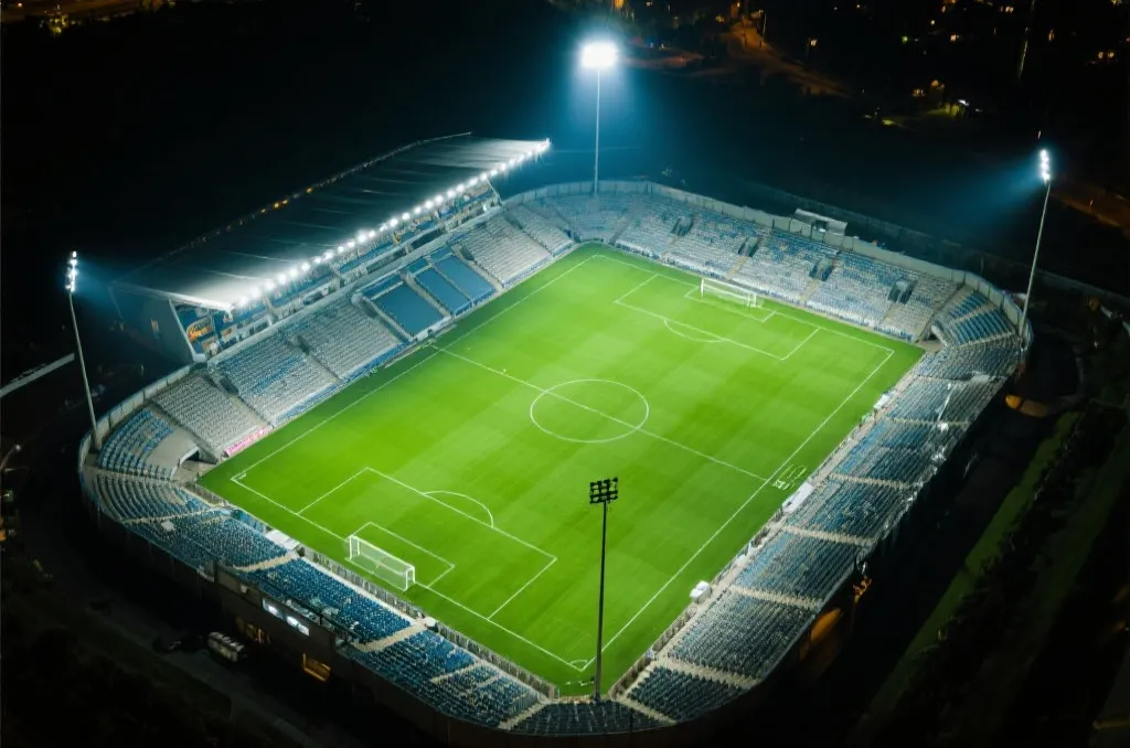 An aerial view of a generic modern football stadium with bright floodlights at night